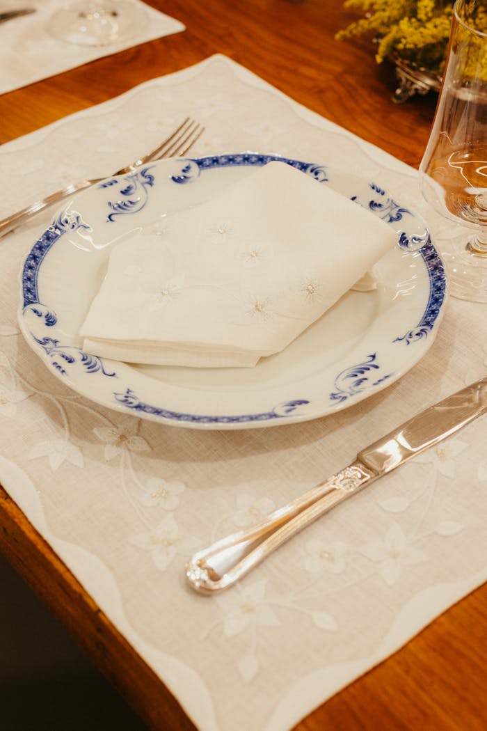 Classic table setting with floral plate, napkin, and silverware on linen placemat.