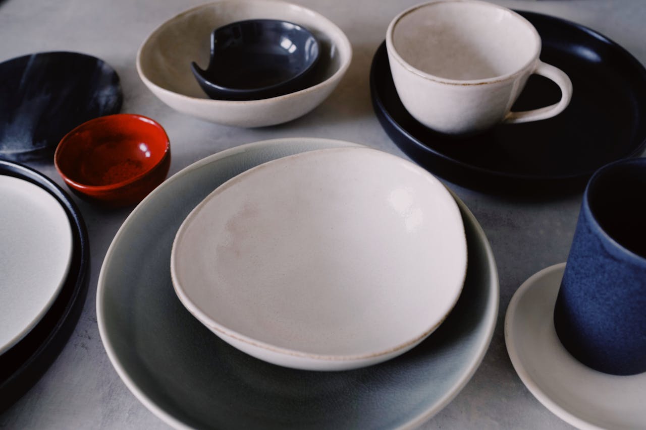 A variety of stylish ceramic dishware including bowls, cups, and plates arranged artistically on a table.